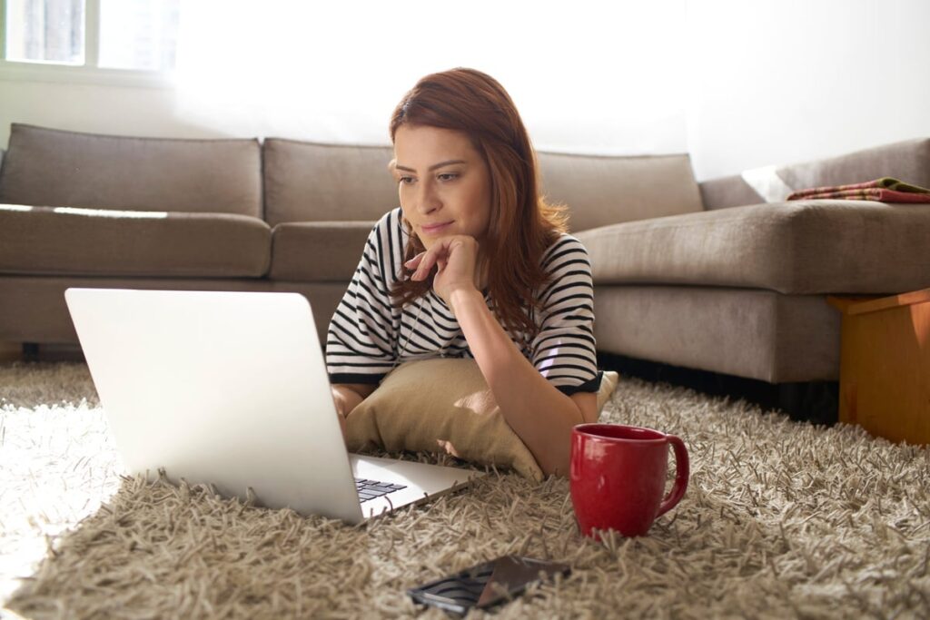 Woman using her laptop on her living room floor C6KDhKx