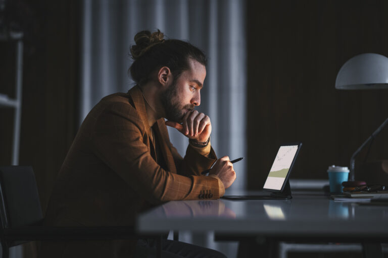 a person in a darkened room looking at stock charts on a tablet