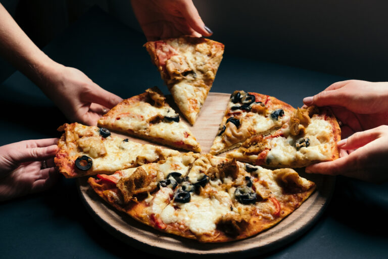 several hands grabbing slices of pizza from a tray