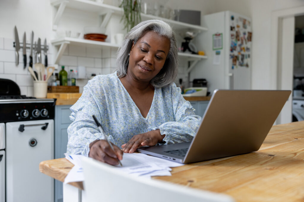 person in kitchen filling out documents in front of her computer