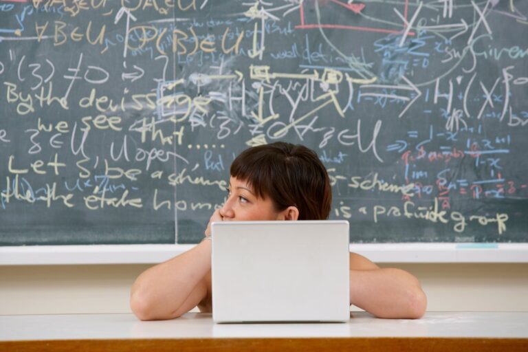 person sits on computer with mathematic equations on chalkboard