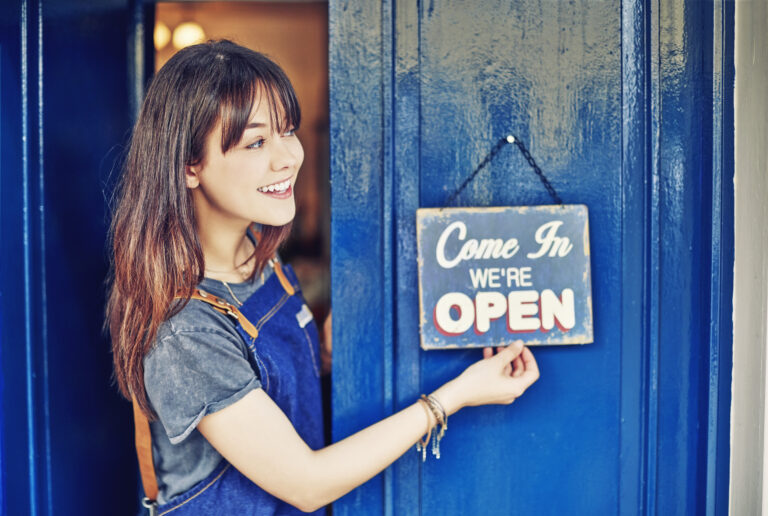 smiling business owner hanging open sign on shop door