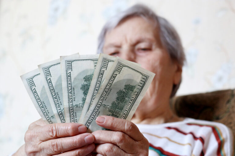 elderly woman retirement social security holding one hundred dollar bills cash getty