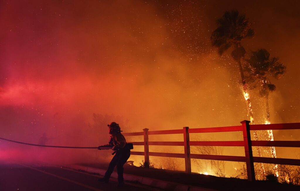 firefighter pulls water hose through fire