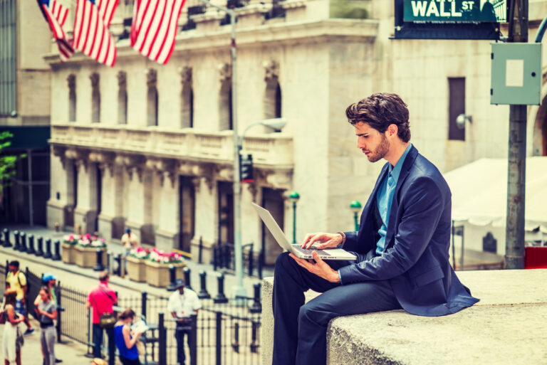 gettyimages man on laptop sitting on ledge across from wall street nyse