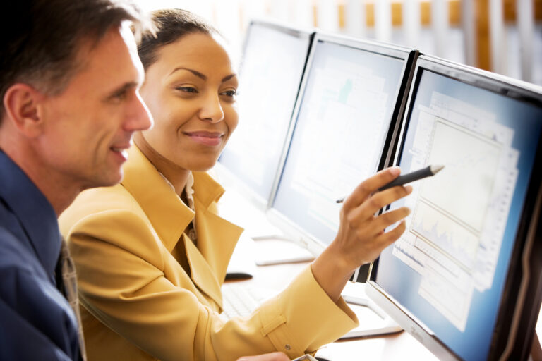 two business people smile while looking at computer data