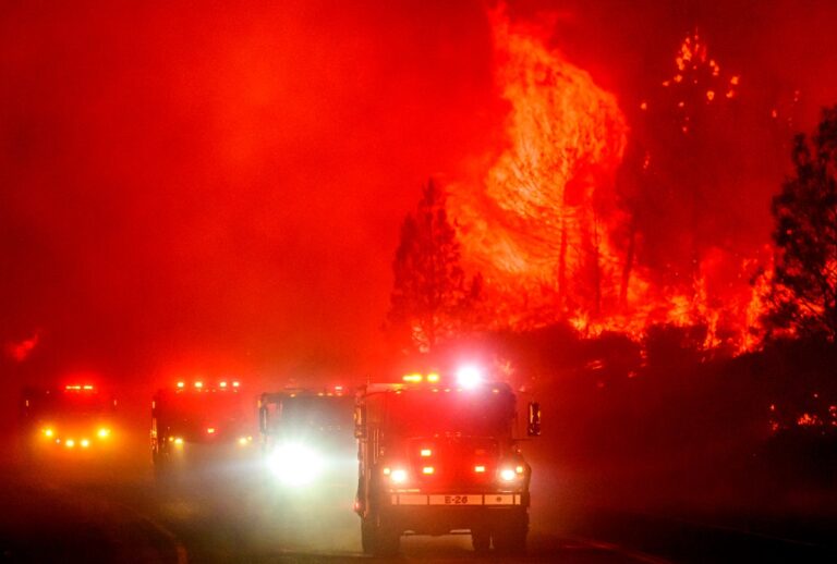 Fire trucks drive through red sky and flames