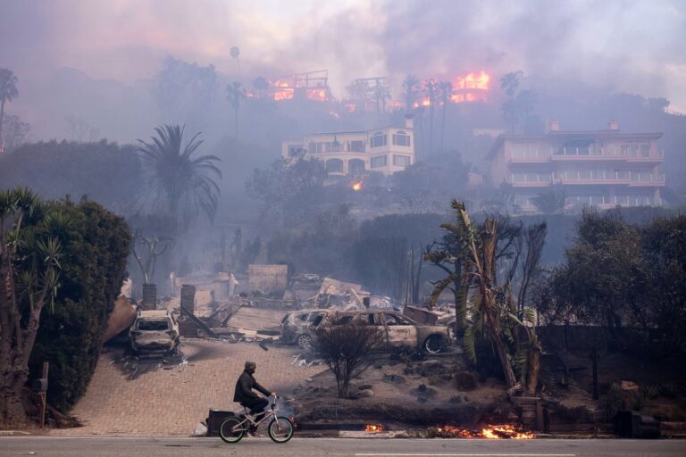 cyclist pedals past burning homes in malibu california