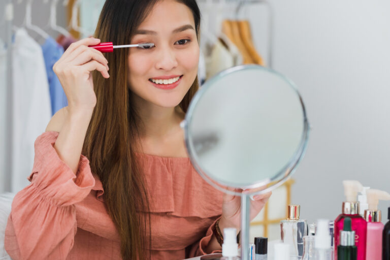 person looking in mirror putting on mascara