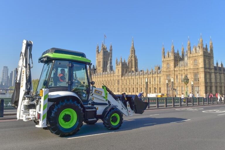 1745995546 a hydrogen jcb digger drives over westminster bridge past houses of parliament