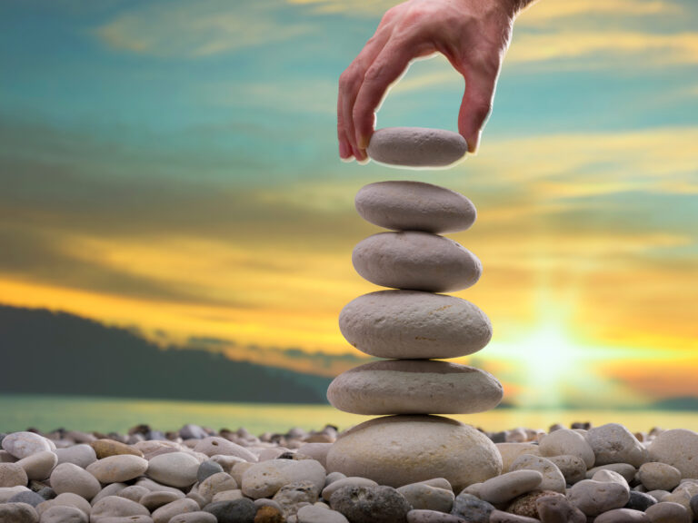 a person stacking stones in a tower with a bright sun in the background